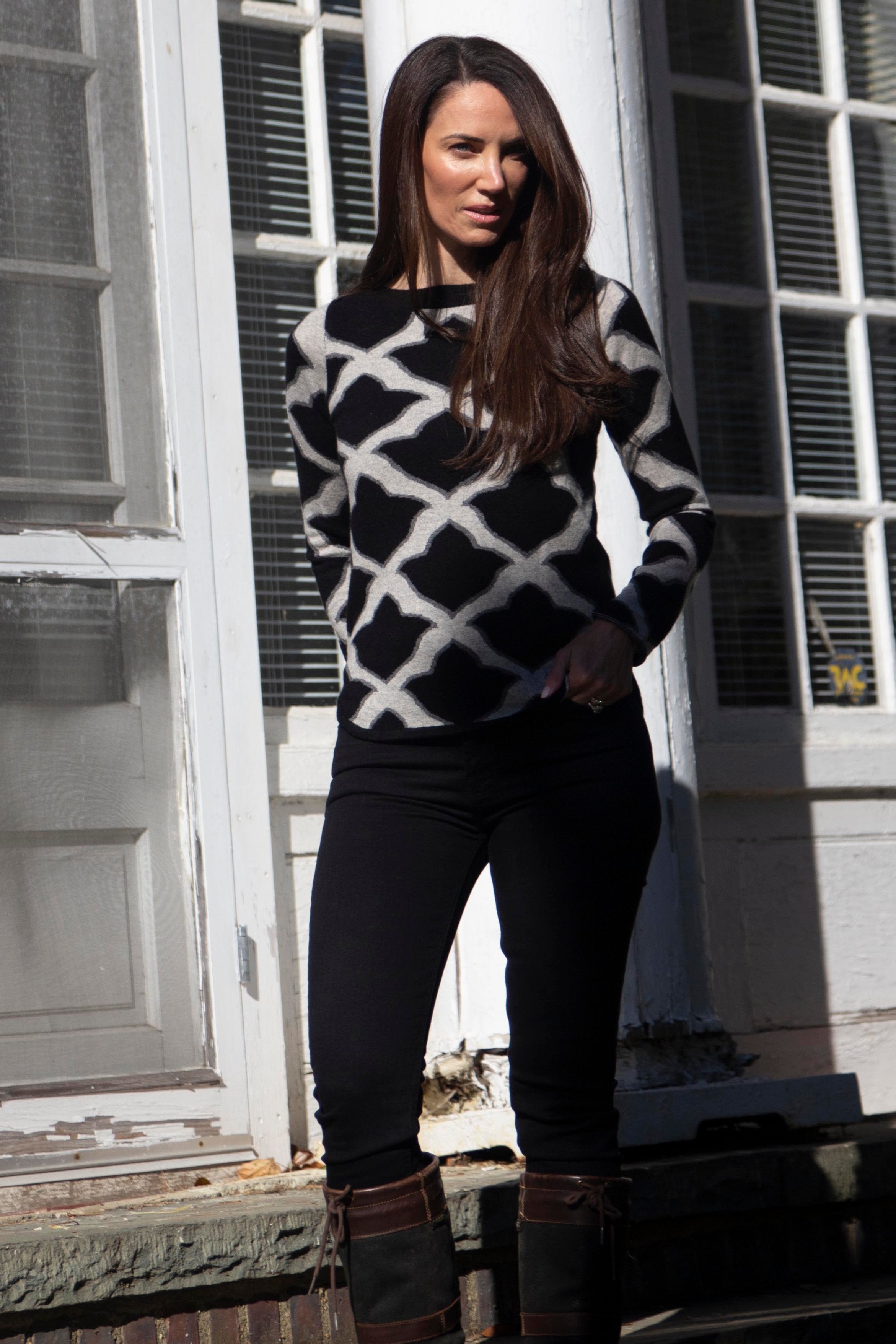 Black ISLEFIELD Fleur De Isle cashmere boatneck pullover displayed on a hanger with a close-up of the fabric texture.