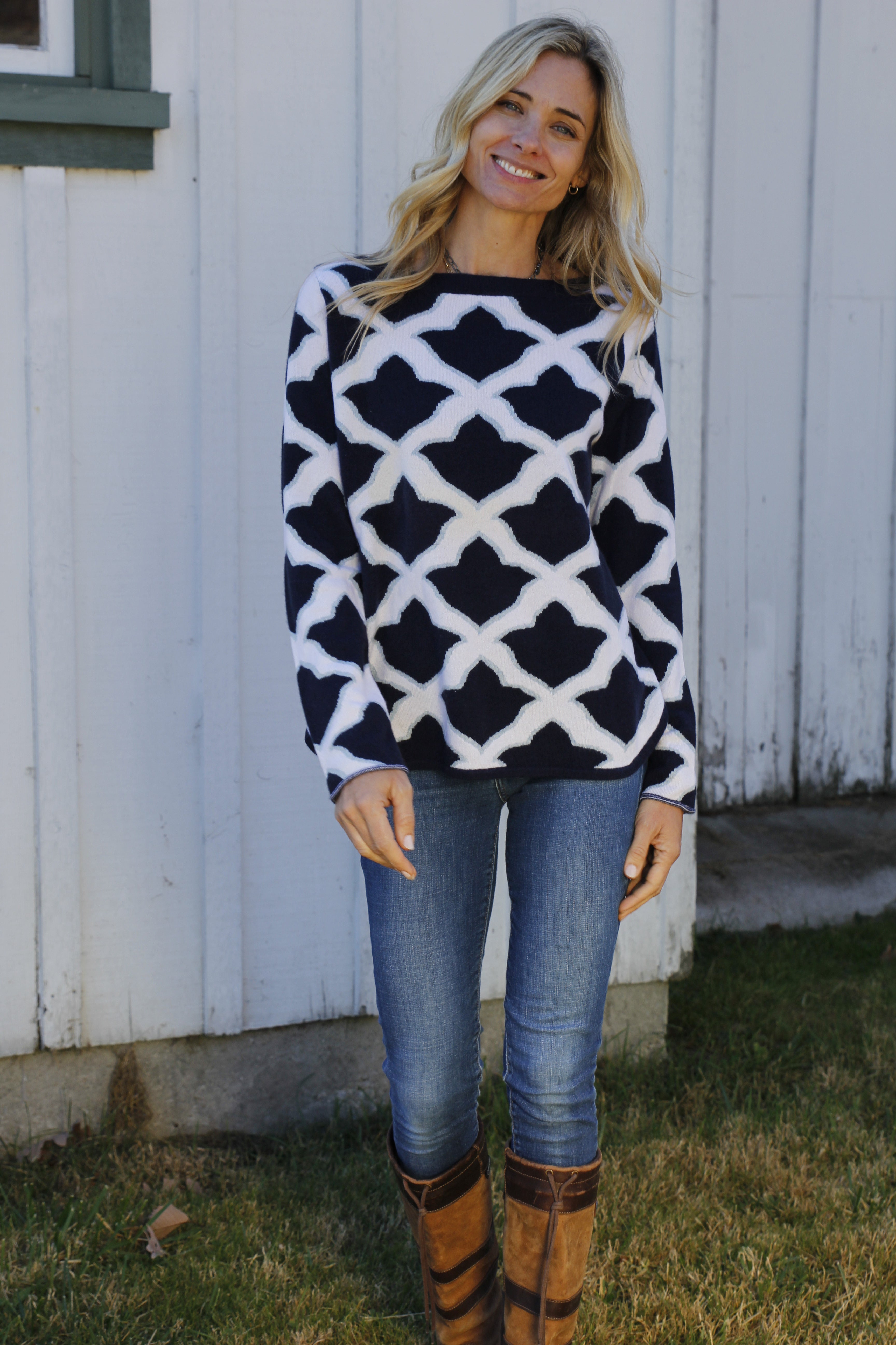 ISLEFIELD Fleur De Isle navy cashmere boatneck pullover displayed on a hanger with a sky background.